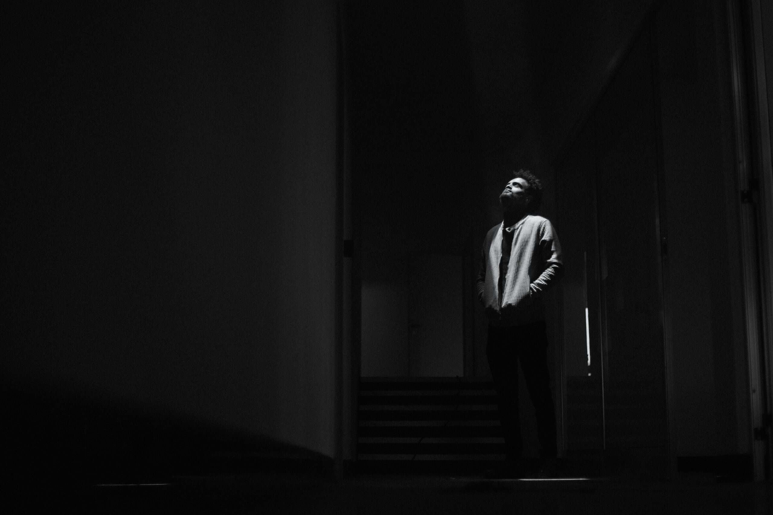 Creator Operating System. Black and white photo of a man standing alone in a dim corridor, evoking solitude.