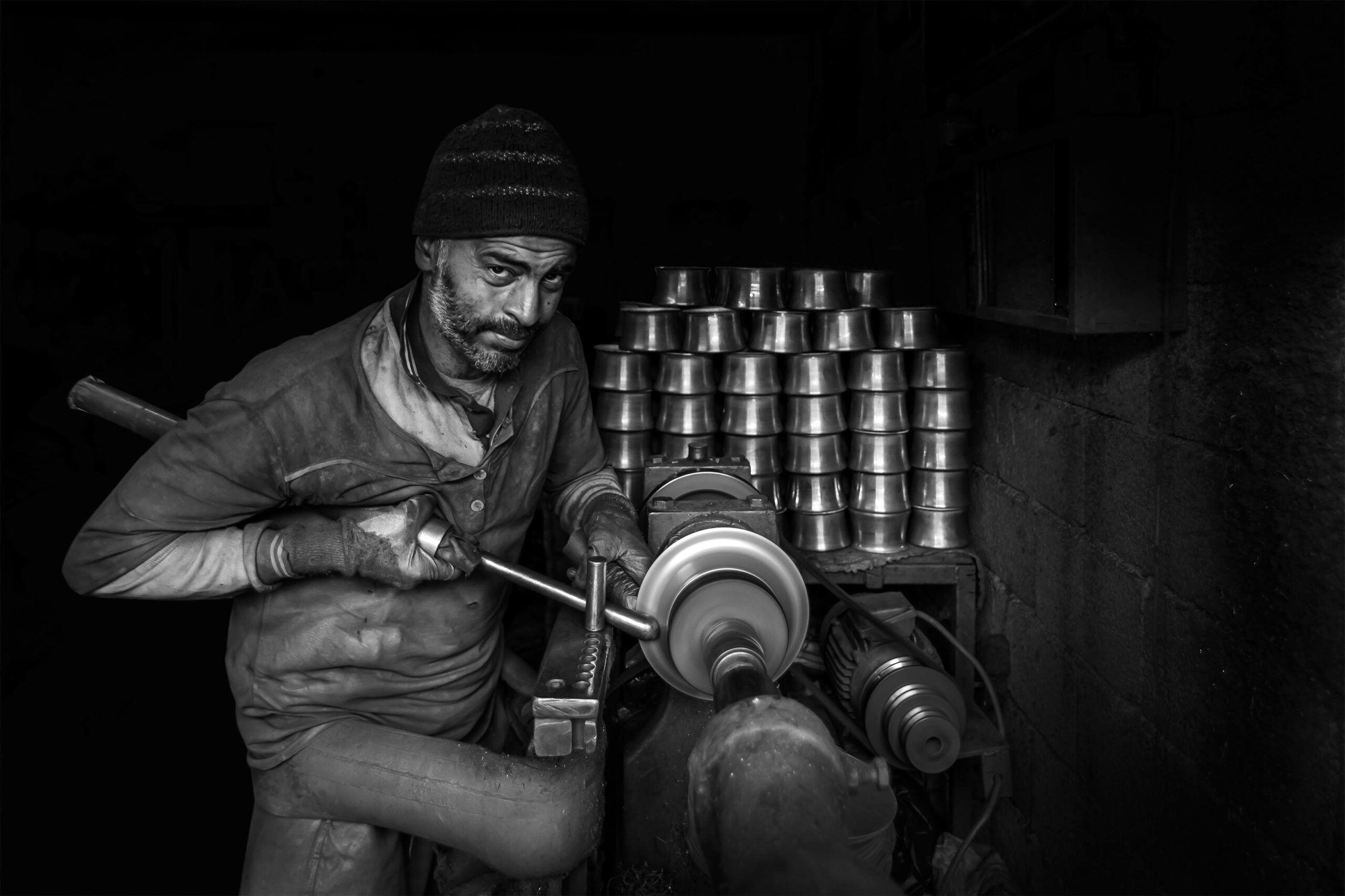 Black and white image of a metalworker using tools in a Turkish factory. Captures industrial craftsmanship.